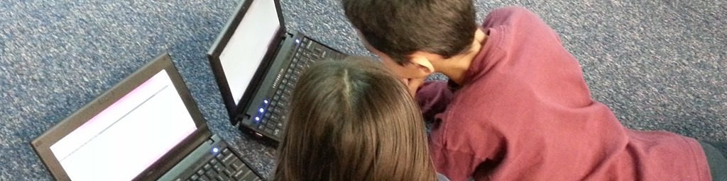 Two kids laying on the floor, each on their own laptop.