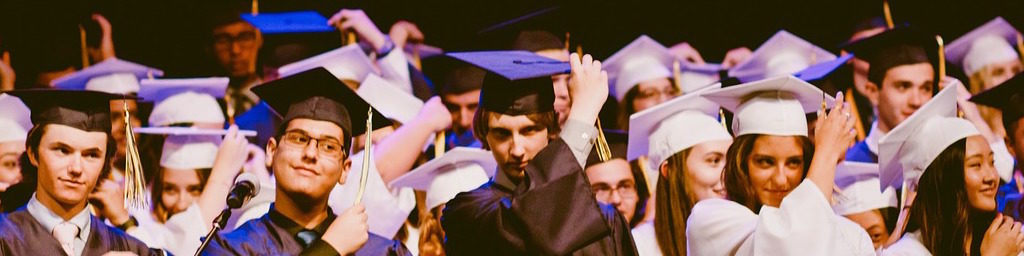 A photo of graduates in caps and gowns moving their tassels from the right to the left. 