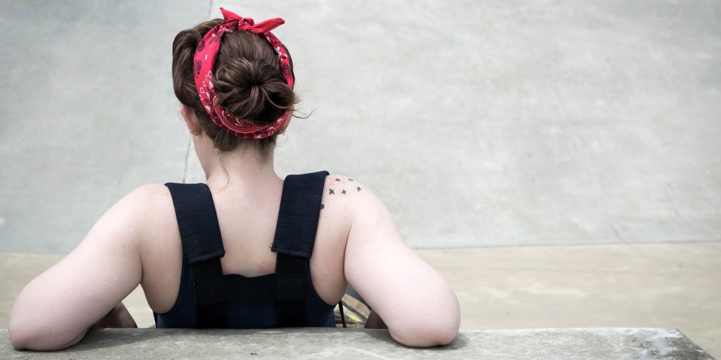A photo of a young woman sitting against a stone bench. Only the back of her is visible.
